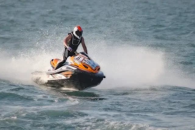 Solo rider in a wetsuit and helmet standing on an orange jet ski at speed